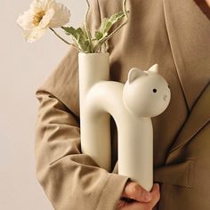 a person holding a vase with a flower in it and a cat figure on the side