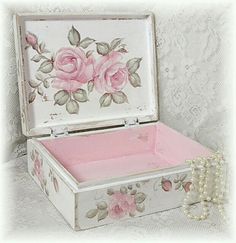 an old white box with pink roses painted on it and pearls hanging from the side