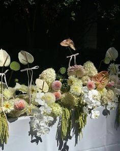 an arrangement of flowers on a table in front of trees