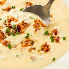 a white bowl filled with soup topped with bacon and green onions next to a spoon