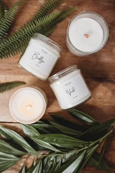 three candles sitting next to each other on top of a wooden table with green leaves