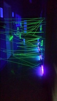 a room filled with green and purple lasers in the dark, while someone is holding their hand out to touch it