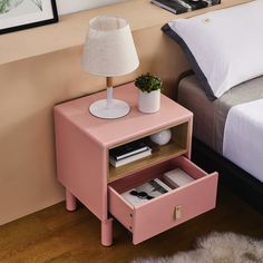 a pink night stand with two drawers and a lamp on it next to a bed