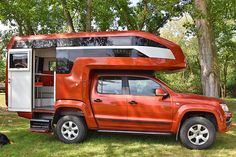 an orange truck with a camper attached to it's bed is parked in the grass