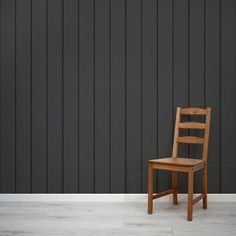 a wooden chair sitting in front of a black wall with vertical stripes on it's side