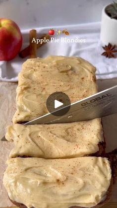 a knife cutting into some food on top of a piece of paper with apples in the background