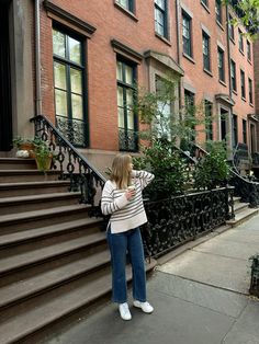 a woman is standing on the sidewalk looking at her cell phone in front of an apartment building