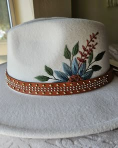 a white hat with flowers on it sitting on top of a table next to a window