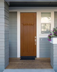 a wooden door on the side of a gray house with flower boxes in front of it