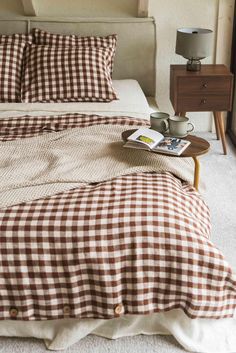 a bed with brown and white checkered comforter next to a night stand on top of it