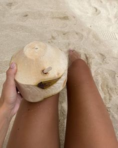 a person is sitting on the beach with their feet in the sand and holding an object