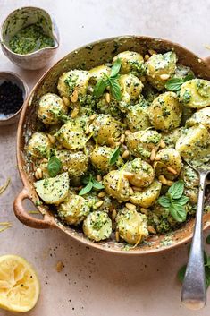 a bowl filled with broccoli and nuts next to some lemon wedges on the side