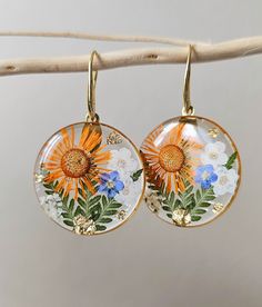 pair of dangle earrings with flowers painted on them hanging from a twig branch