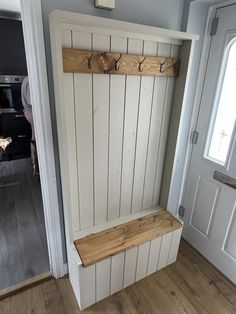 a wooden bench sitting in front of a white door with hooks on it's sides