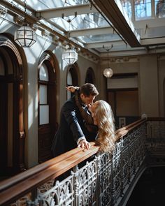 a man and woman standing on top of a balcony next to an iron railing with windows