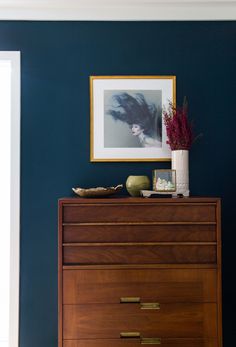 a wooden dresser sitting in front of a blue wall with a painting on the wall