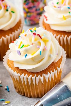 cupcakes with white frosting and sprinkles next to a knife