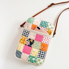 a multicolored patchwork cross body bag on a white surface with a brown strap