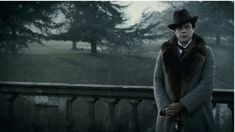 a man in a coat and hat standing on a balcony