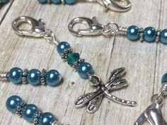 some blue beads and silver charms on a wooden table with a dragonfly charm hanging from it's side