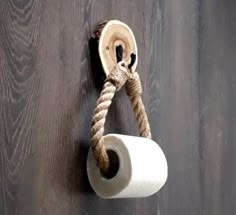 a rope wrapped around a toilet paper holder on a wood floor with a knot hanging from it