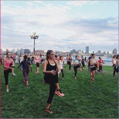 a large group of people are doing yoga in the grass by the water and buildings