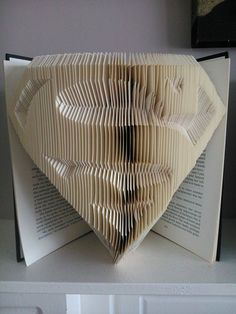 an open book with folded pages in the shape of a heart, sitting on top of a shelf