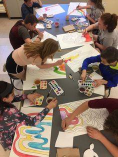 a group of people sitting around a table with art supplies on it and coloring paper in front of them