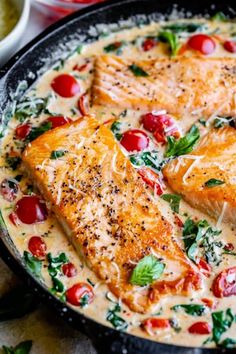 two fish fillets in a skillet with tomatoes and spinach on the side