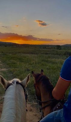 two people riding horses on a dirt road at sunset in the distance is a field with grass and trees