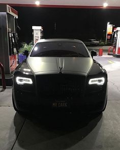 a black car parked in front of a gas station at night with its lights on