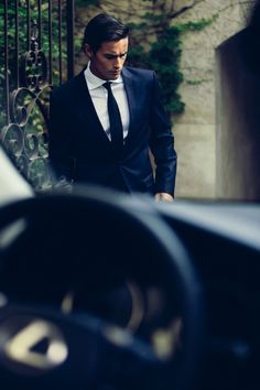 a man in a suit and tie walking up steps to an iron gate with ivy growing on it