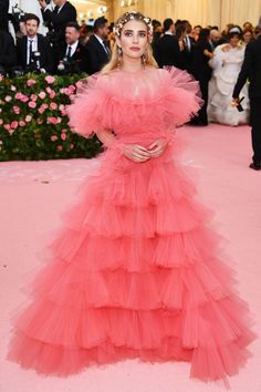 a woman in a pink gown standing on a pink carpet with other people behind her