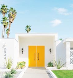 a yellow door is in front of a white house with palm trees and green grass