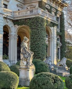 an ornate building with statues in front of it and green bushes around the entrance area