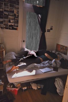 a woman laying on top of a bed in a room with lots of clutter