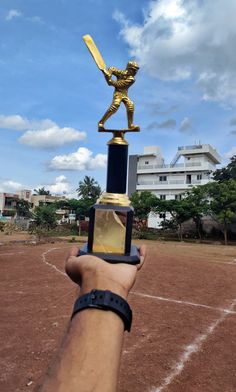 a hand holding up a gold trophy with a baseball player on it's arm