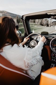 a woman sitting in the driver's seat of an orange sports car driving down a road