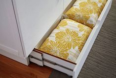 an open drawer with two yellow pillows in it and a rug on the floor next to it