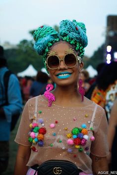 a woman with bright blue eyes and green hair wearing sunglasses, holding a black purse