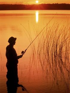 a man standing in the water while holding a fishing pole