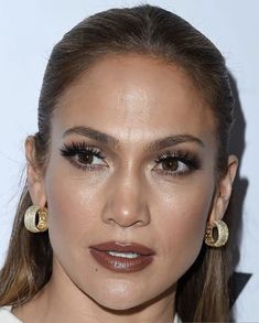 a close up of a person wearing large earrings and makeup on her face with brown eyeshadow