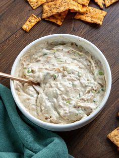 a white bowl filled with dip surrounded by tortilla chips on a wooden table