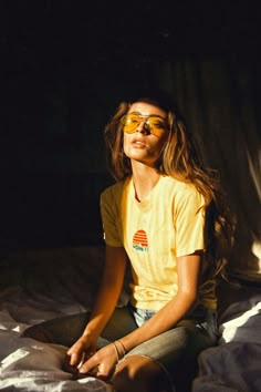 a young woman sitting on top of a bed wearing sunglasses and looking off to the side