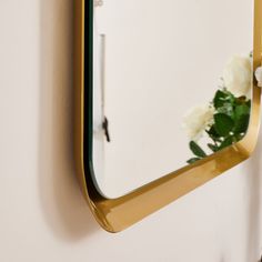 a mirror hanging on the side of a wall with white flowers in front of it