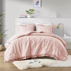 a bed with pink comforter and pillows in a room next to a potted plant