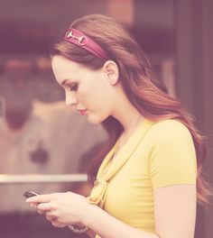 a woman in a yellow shirt is looking at her cell phone while wearing a pink headband