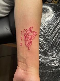 a small butterfly tattoo on the left inner arm, with two numbers and one is red