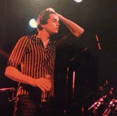 a man standing in front of a microphone on stage with his hand to his head