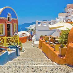 an alley way with colorful buildings and umbrellas on the side, in front of blue water